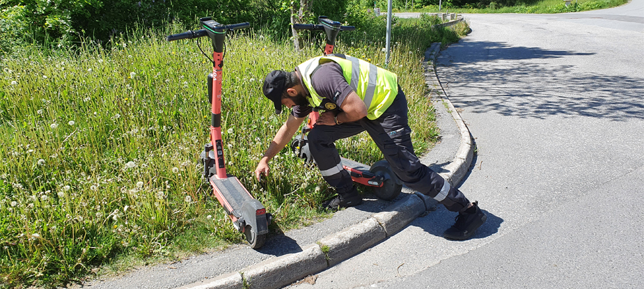 parkeringsvakt som kontrollerar parkerad elsparkcykel med hjälp av smartphone