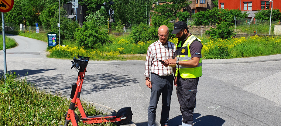 parkeringsvakt som visar något på en smartphone för en man framför en elsparkcykel